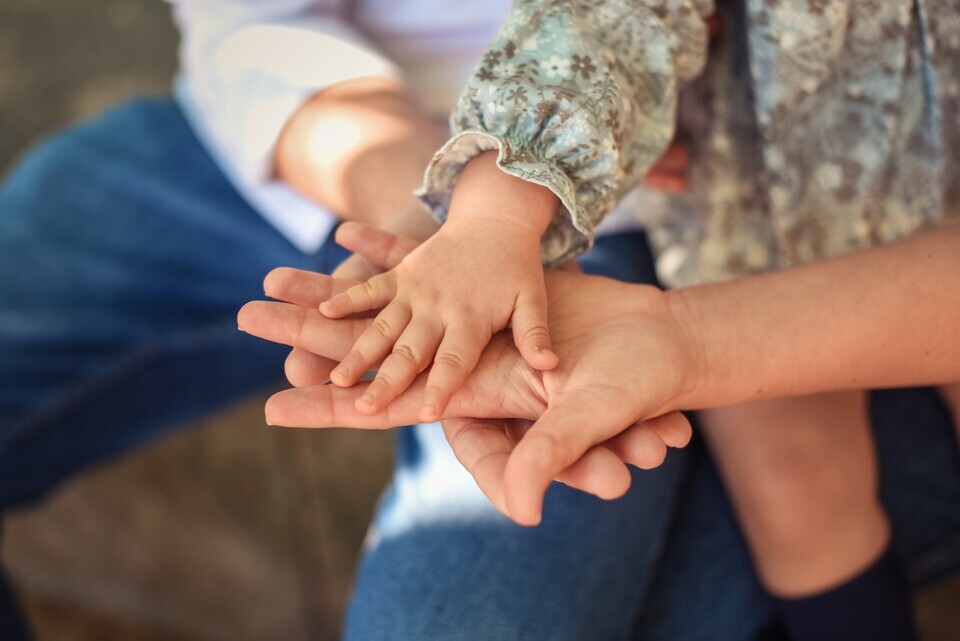 Mãos de adultos e uma criança se unindo em um gesto de carinho.