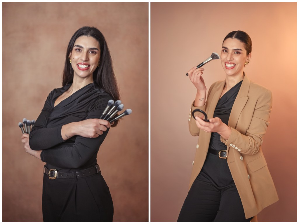 Uma mulher sorridente segurando pincéis de maquiagem com uma blusa preta em um fundo marrom.